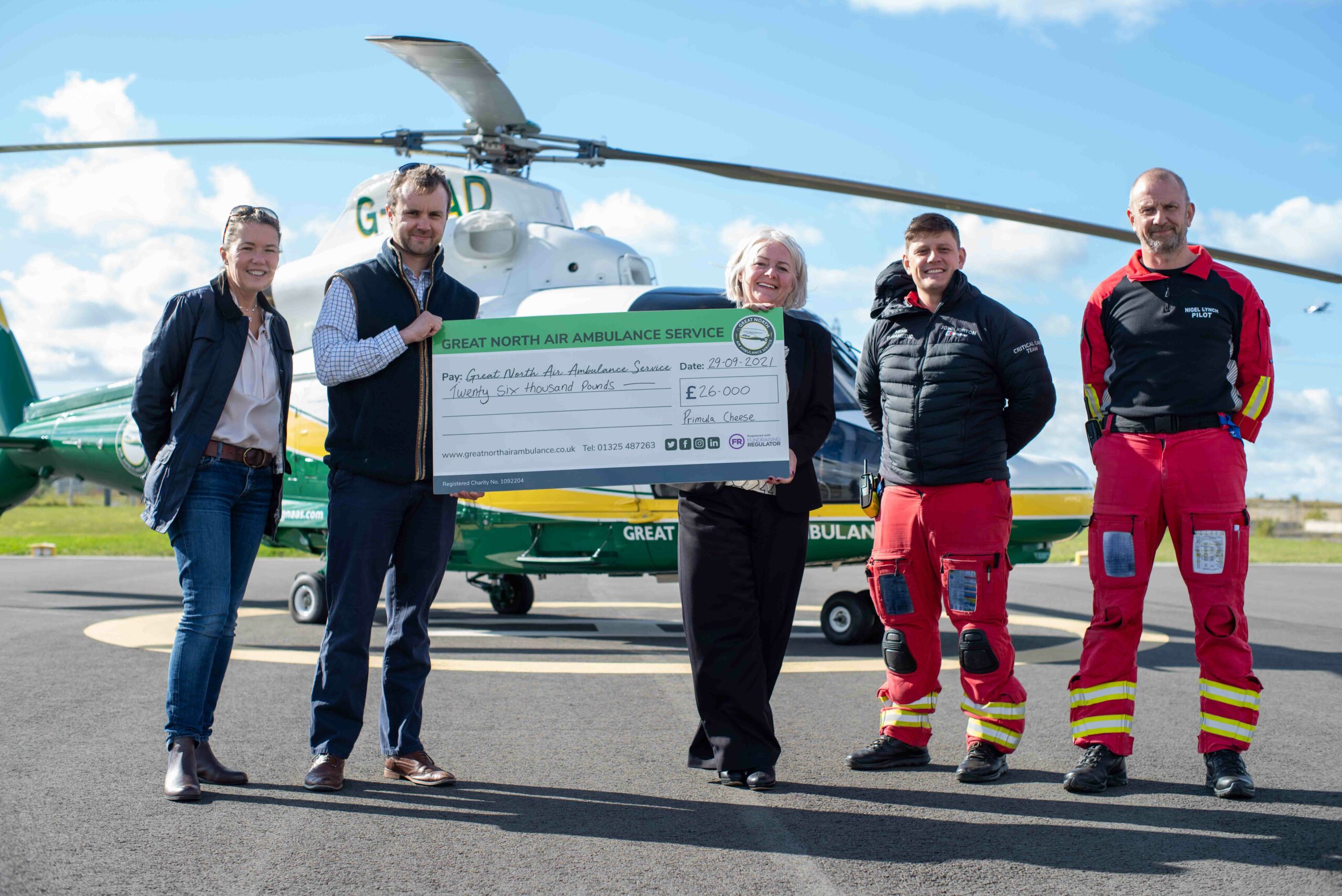 Primula staff presenting a cheque to Great North Air Ambulance with helicopter in the background